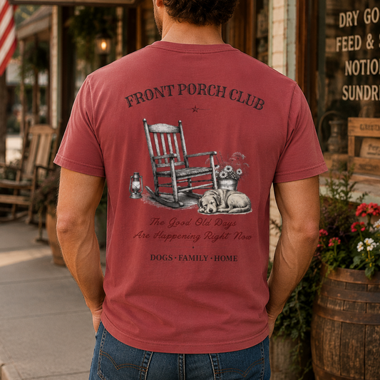 A man wearing a dusty rose red t-shirt with a detailed dog-themed graphic on the back, standing on a rustic street in front of a General Store.