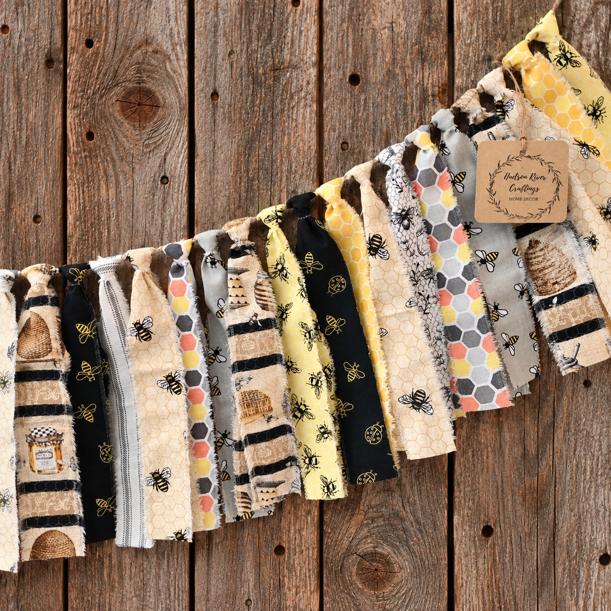 A fabric bunting banner with various honeybee and beehive-themed patterns in yellow, black, beige, and gray, hung diagonally on a rustic wooden plank background. 
