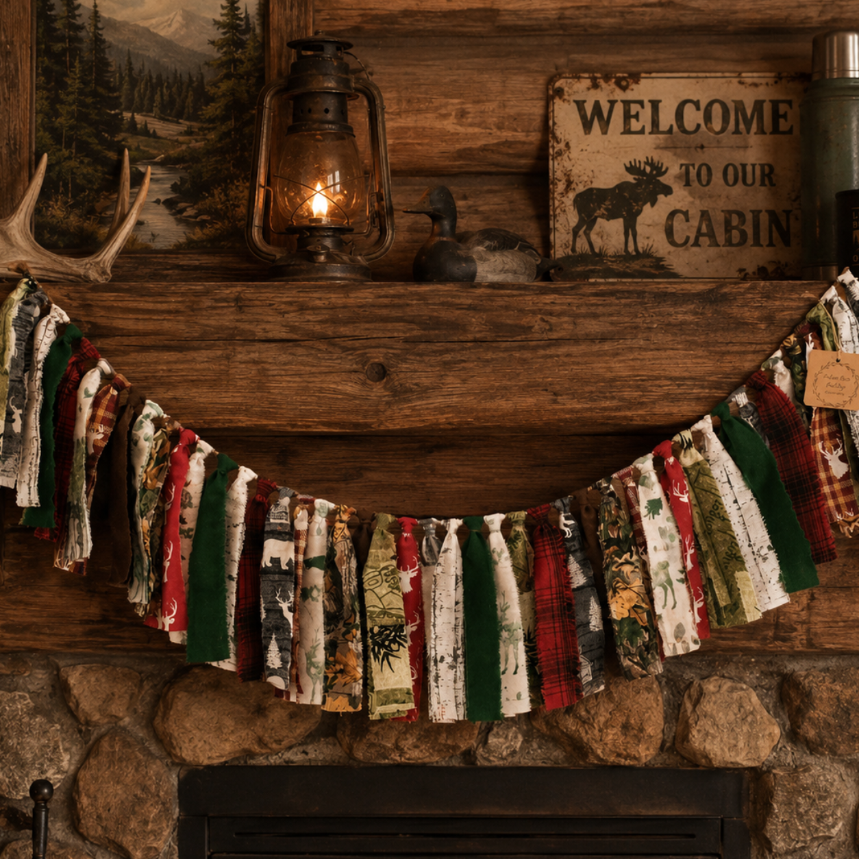 A rustic fabric garland with vertical strips of red, green, white, and camouflage-patterned material hangs across a wooden fireplace mantel in a cabin setting, with a lantern, framed mountain scene, antlers, and a rustic sign above it.
