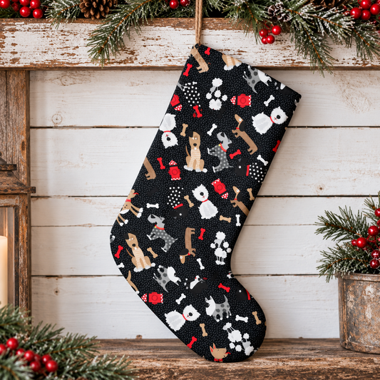 A black Christmas stocking with a dog-themed print of various dog breeds, bones, and paw prints, hanging on a rustic wooden mantel decorated with pine branches and red berries.