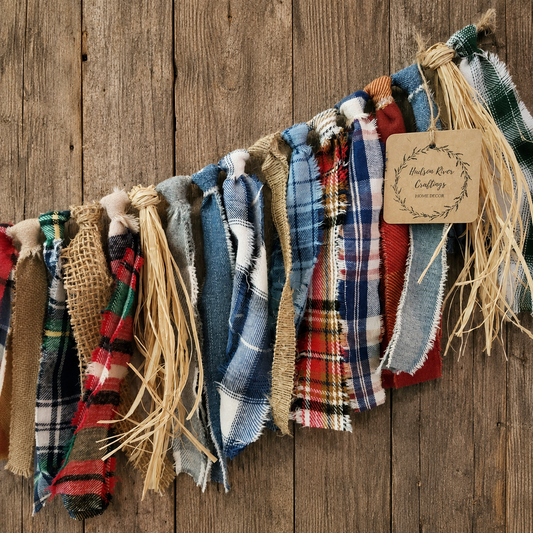 A rustic fabric garland made of assorted plaid and burlap ribbon strips hanging against a weathered wood plank background. 