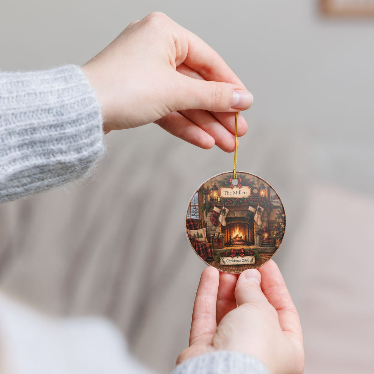 A person holds a round Christmas ornament featuring an illustration of Santa in his study, with a gold hanging string, against a soft, blurred indoor background.