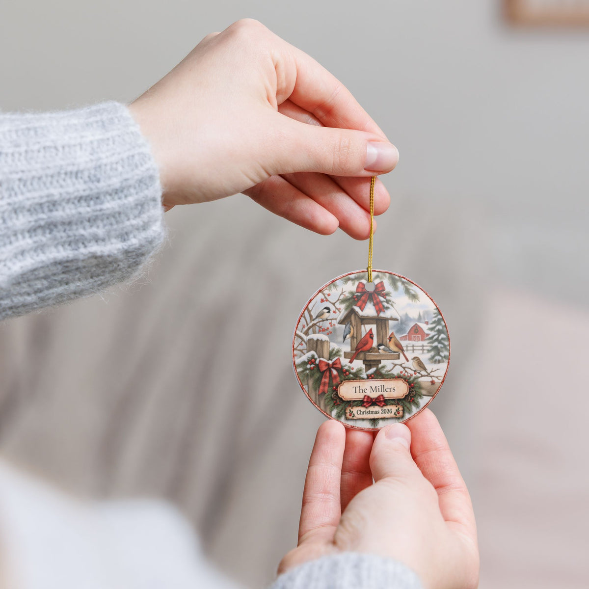 A person holds a round Christmas ornament featuring a winter village scene.