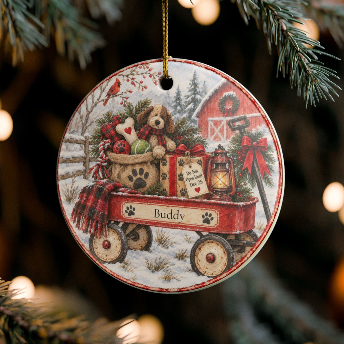 A round ceramic Christmas ornament hanging from a pine tree branch. The ornament features a vintage-style illustration of a red wagon carrying a teddy bear, gifts, and a lantern, with the name 'Buddy' printed on it.