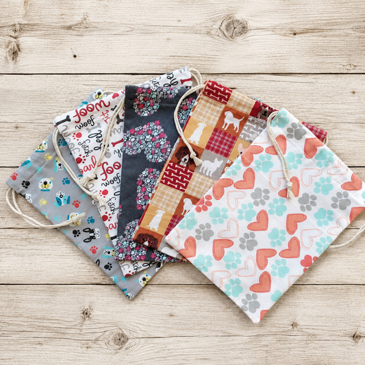 Fabric drawstring pouches with different pet-themed patterns, including hearts, paw prints, and dog silhouettes, arranged on a light wood background.