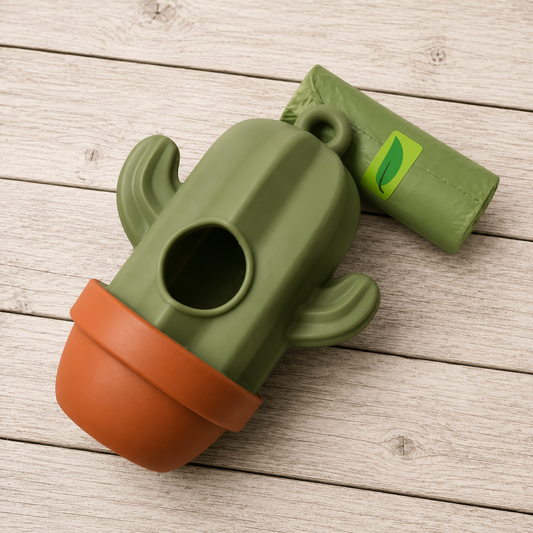 An olive green cactus-shaped pet poop bag holder with an orange-brown pot base, shown next to its matching green bag on a light wood plank surface.